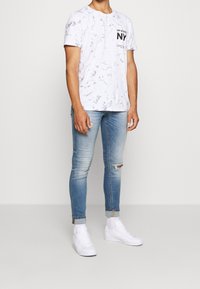 Vit t-shirt med marmormönster och svart text, matchad med ljusblå skinny jeans med rivna knän och vita sneakers.