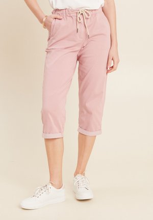 Lichtroze cropped broek met een elastische tailleband en trekkoord, met opgerolde manchetten en zijzakken. Gecombineerd met witte sneakers.