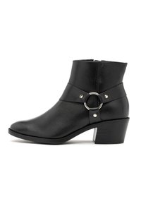 Bottine en cuir noir avec un petit talon carré, une sangle décorative et un détail en anneau argenté sur le côté, sur fond blanc.
