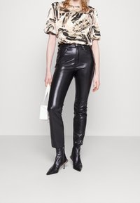Pantaloni aderenti in ecopelle nera, una blusa corta a maniche corte con motivo in rosa e nero, e stivaletti con punta. Tieni una borsa bianca.