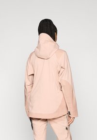 Casaco impermeável rosa claro com capuz, apresentando um corte descontraído, mangas longas e detalhes em painel texturizado contrastante.