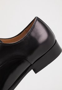 Gros plan sur le talon et la semelle d'une élégante chaussure de ville en cuir noir, avec des coutures visibles et une finition lisse et polie.