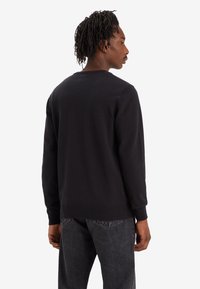 Sweatshirt noir à manches longues avec un col rond, des poignets et un ourlet côtelés. Présente une texture lisse et une coupe décontractée, associé à un jean noir.