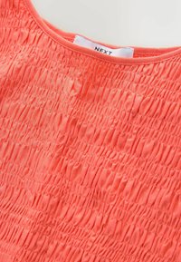 Korallikarva triibuline pluus koos ümarkaelusega, millel on kogu pinnal kogutud tekstuur. Sildi peal kaelas sees on kiri "NEXT".