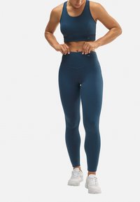 Sujetador deportivo de color azul oscuro y leggings de tiro alto a juego, fabricados con un material suave y elástico. Un par de zapatillas deportivas blancas completan el conjunto.