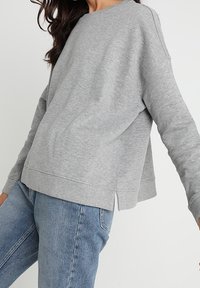 Grå, lätt sweatshirt med avslappnad passform, rund halsringning och sidorevor. Bomullsblandat material ger en mjuk textur.
