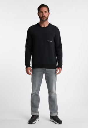 Felpa nera con tasca frontale e logo bianco. Indossata con jeans grigi chiari e sneakers nere con accenti rossi.