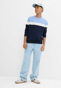 Maglione a righe blu navy e azzurro, jeans azzurri a vestibilità comoda e sneakers bianche con dettagli neri. Un cappellino azzurro completa il look.