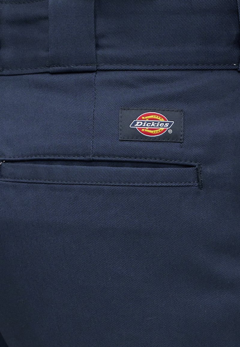 Marineblauer Stoff mit einer Gesäßtasche und einem aufgenähten Dickies-Logo-Patch mit rotem und gelbem Kreis.