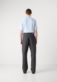 Lyseblå kortærmet skjorte parret med mørkegrå løst sidende jeans med en blå label i livet, der viser et afslappet design.