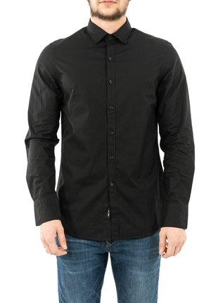 Camisa negra de manga larga hecha de tela sólida, con cuello, cierre de botones y un diseño ajustado. Combinada con jeans azules.