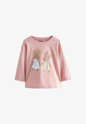 Roza bombažna srajca z dolgimi rokavi, ki na sprednji strani prikazuje dva šivana zajca z različnimi teksturami, oblečena v svetlo modra in bele obleke.