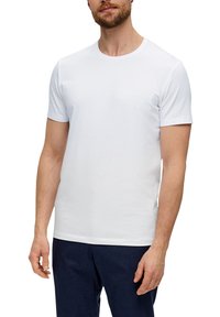 Camiseta blanca de manga corta de algodón, con cuello redondo y una textura suave, combinada con pantalones oscuros.