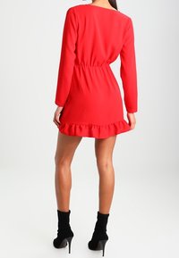 Vestido rojo con mangas largas, cintura elástica y dobladillo con volantes. Combinado con botas negras hasta el tobillo. Textura suave, diseño simple.