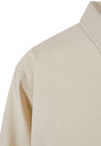 Tissu de chemise beige en gros plan montrant un col pointu et une couture d'épaule sur un fond uni.
