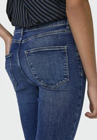 Mörkblå denimjeans med slim fit, subtila slitningar, två bakfickor och medelhög midja. Tyget har en lätt stretch.