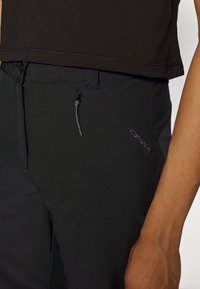 Svarta träningsbyxor med en slät textur, dragkedjeficka, justerbar dragsko och sydda detaljer vid midjan.