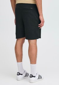 Pantalones cortos de sudor negro con un ajuste relajado, cintura elástica y bolsillo trasero, combinados con zapatillas blancas y calcetines de longitud media.
