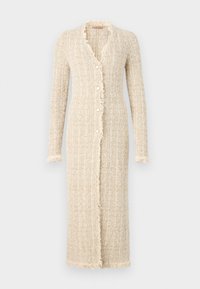 Long gilet beige en tissu tricoté texturé. Présente un bord effiloché, une fermeture à cinq boutons et des manches longues.