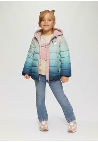 Puchowa kurtka w gradientzie od jasnoszarego do turkusowego, z różowym wyściółką, naszywką w kształcie serca, noszona na jasnym swetrze i dżinsach, w zestawieniu z trampkami.