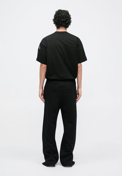 Czarny, oversize t-shirt z krótkimi rękawami; połączony z fakturowanymi czarnymi spodniami. Widok z tyłu pokazuje prosty design oraz luźny krój, bez widocznych logo.