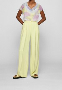 Haut transparent de couleur pastel avec manches bouffantes ; pantalon taille haute à jambes larges en jaune doux  ; sandales compensées avec semelles noires.