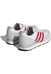 Sportschuhe mit einem weißen Obermaterial, grauem Absatz und Sohle, die an den Seiten drei rote Streifen und eine Schnürung aufweisen. Glatte Textur.