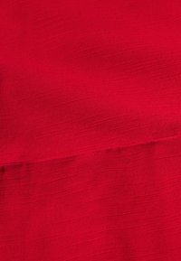 Crvena teksturirana tkanina s finim horizontalnim linijama. Materijal izgleda lagano i blago sjajno, pogodan za odjeću ili tapeciranje.
