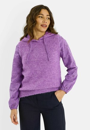 Jersey de punto color lavanda con capucha, cuerpo texturizado y mangas largas con relieve floral. Combinado con pantalones oscuros de rayas finas.