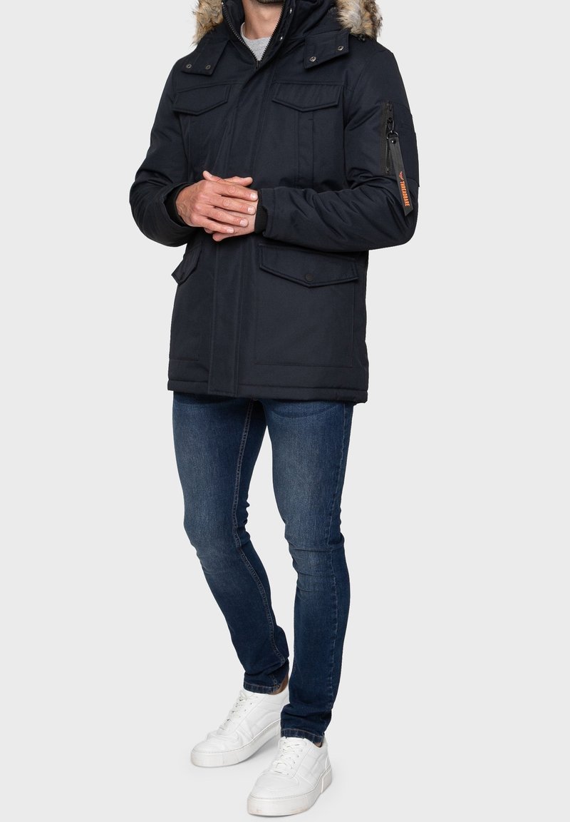 Námořnická parka s kapucí z umělé kožešiny, s kapsou na zip na prsou, dvěma předními klopovými kapsami a elastickými manžetami. Nositelná přes upnuté džíny a bílé tenisky.