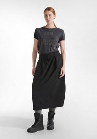 Černá sukně s sklady, odpovídající šedé tričko s potiskem "JSEM SVOU VLASTNÍ MUZOU" a černé boty na šněrování. Hladká tkanina, neformální design.