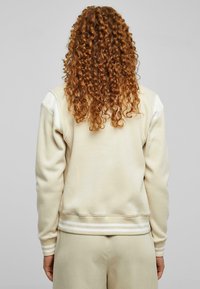 Beige genser med rund hals og stripete ribbestrikket kant. Har lange ermer med kontraststoff på skulderen.