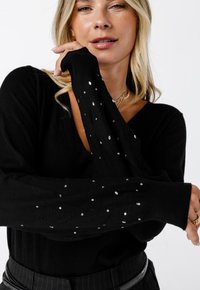 Zwarte lange mouwen sweater gemaakt van een zachte stof, met een V-hals en versierd met verspreide zilveren rhinestones op de mouwen.