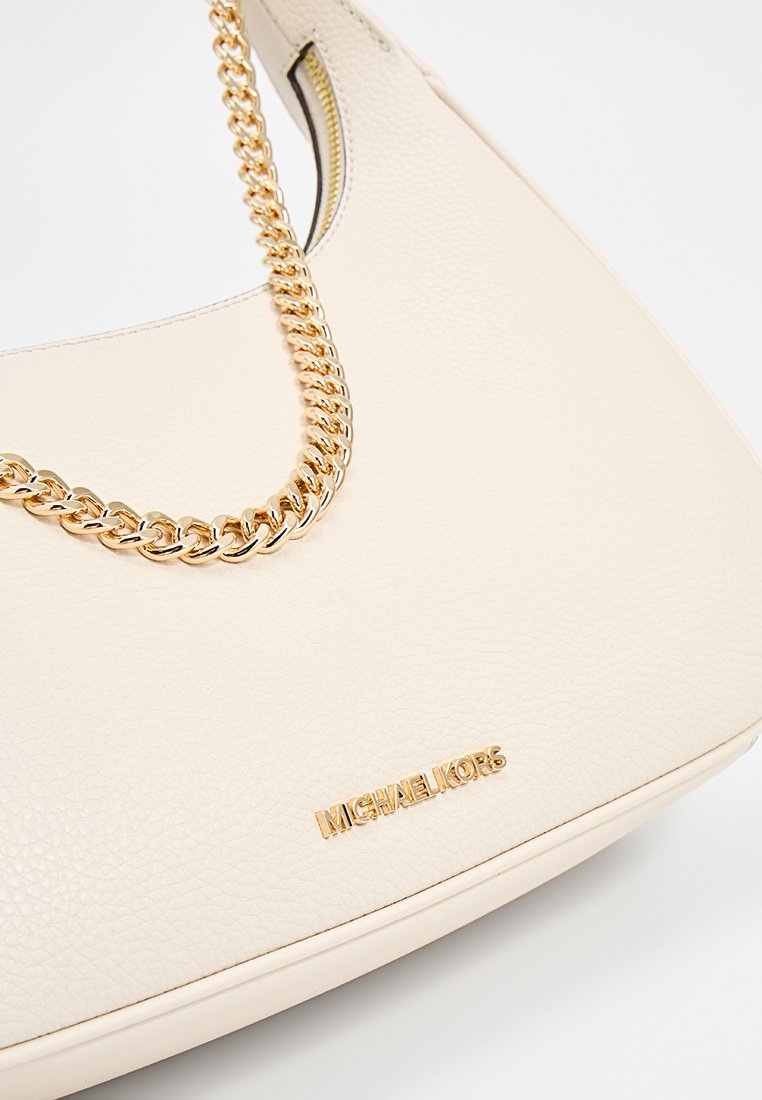 Sac à main en cuir crème avec un design arrondi, doté d'une chaîne dorée et d'un accent logo doré à l'avant. Surface texture lisse.