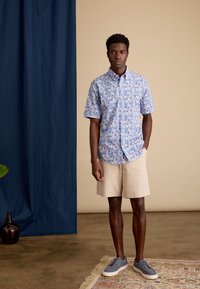 Korte mouwen overhemd in het blauw met een bloemenpatroon, gecombineerd met beige shorts en grijze schoenen. Gladde stof en een ontspannen pasvorm.