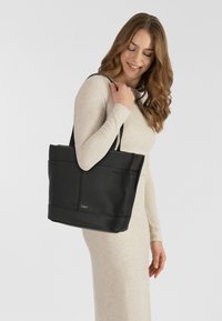 Borsa tote in pelle nera con superficie texturizzata, due manici superiori e tasche esterne. Logo visibile sulla parte anteriore inferiore.