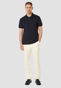 Marineblauwe polo met een zachte textuur en een knoopsluiting met drie knopen, gecombineerd met crèmekleurige broeken en zwarte loafers. Eenvoudige, moderne pasvorm.