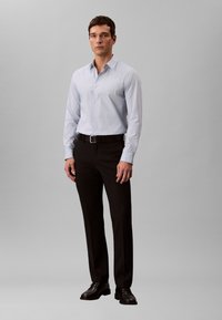 helehall sinine nööbitav särk, mustad pidulikud püksid ja mustad kingad; lõige on kohandatud, pikad varrukad, sile kangas, minimaalne detailide arv.