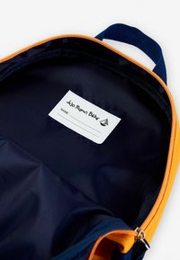 A kék és narancssárga hátizsák belseje sima, tartós anyagból készült, névtáblának is van helye benne. Cipzáras záródás és erős fogantyú tartozik hozzá.