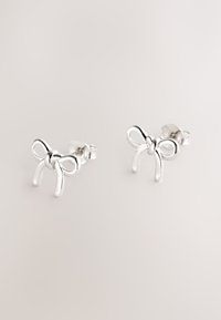 Naušnice od srebra u obliku mašna, s glatkom teksturom i zaobljenim rubovima, s poliranim i reflektirajućim površinama.