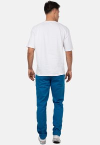 Witte T-shirt met korte mouwen, gecombineerd met blauwe broek, met een relaxte pasvorm en rechte snit. De outfit wordt afgemaakt met witte sneakers.