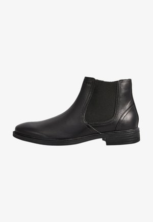 Bottes noires en cuir montantes avec des panneaux latéraux élastiques, un bout arrondi et un petit talon empilé. Texture lisse avec un décor minimal.