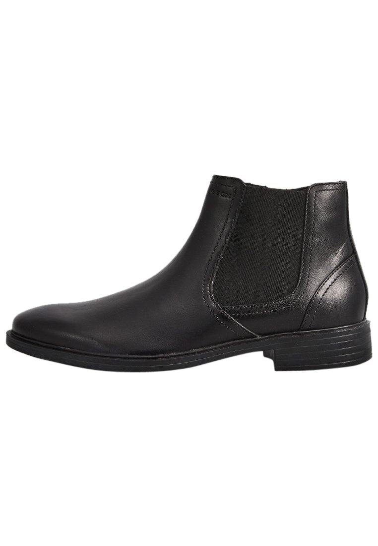 Botas de piel negra a los tobillos con paneles laterales elásticos, puntera redondeada y un tacón bajo apilado. Textura suave con un diseño minimalista.