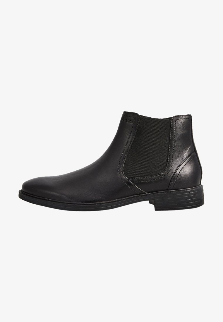 Botas de piel negra a los tobillos con paneles laterales elásticos, puntera redondeada y un tacón bajo apilado. Textura suave con un diseño minimalista.