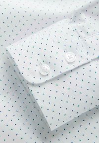 Poignet de chemise blanche avec un petit motif à pois bleus et verts et deux boutons blancs sur le poignet.
