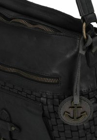 Zwarte leren handtas met een rits aan de voorkant, een geweven textuurvlak en een ronde ankerembleem dat aan de ring van de schouderband hangt.