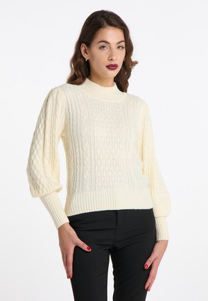 Pulover crem cu tricotaj tip cablu, cu guler înalt cu nervuri și mâneci bufante; prezintă modele texturate și un tiv ajustat. Purtați-l cu pantaloni negri.