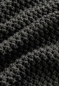 Strukturiertes schwarzes Gewebe mit einem gewebten Muster, das eine weiche und leicht flauschige Oberfläche aufweist und ein geschichtetes, räumliches Erscheinungsbild erzeugt.