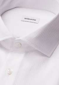 Witte overhemd met een geweven patroon, voorzien van een label met de tekst "seidensticker" en een knoopsluiting bij de kraag.