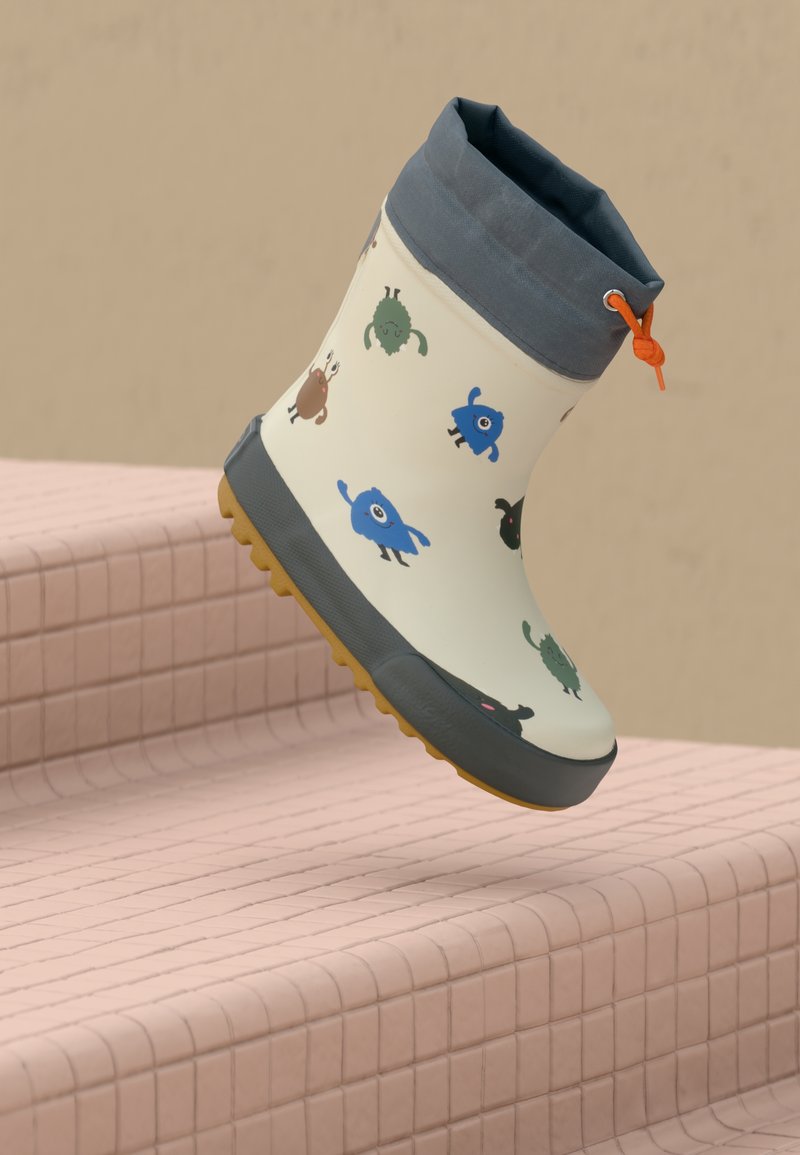 Bottes de pluie pour enfants avec des imprimés de monstres colorés en cartoon, une bordure grise, un cordon orange et une semelle jaune texturée, placées sur des marches carrelées roses.